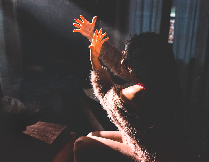 A woman in a fluffy sweater reaches her hands into a beam of light.