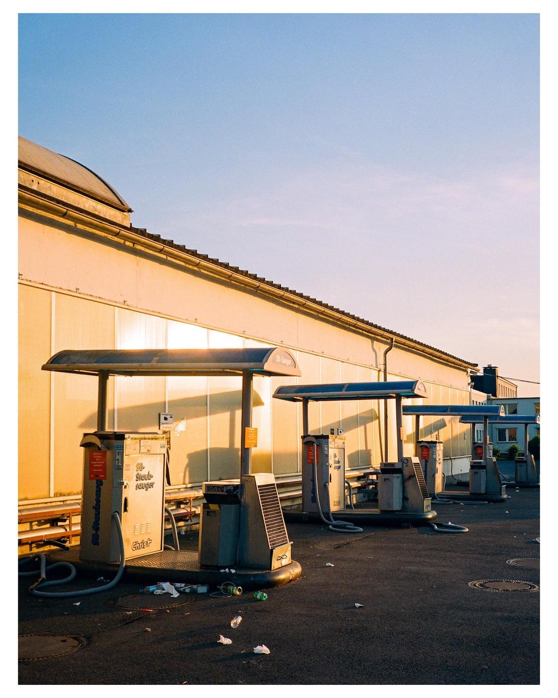 A row of self-service car wash vacuum cleaners stands in front of a building at sunset.