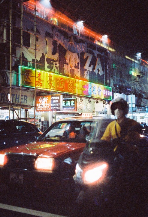 A street at night is filled with cars and neon signs.