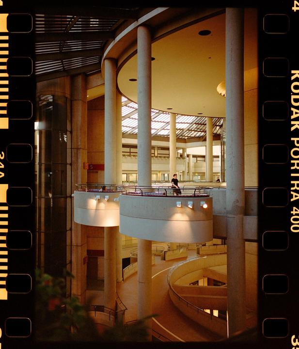 A man stands on a balcony overlooking a multi-story interior space with circular walkways and a skylight.