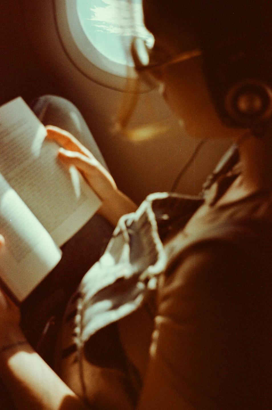 A person is reading a book next to an airplane window.