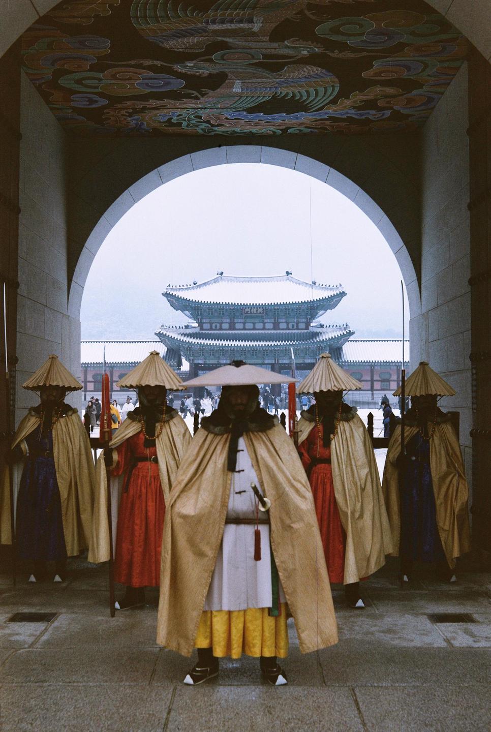 Five royal guards stand in an archway with a snow-covered palace in the background.