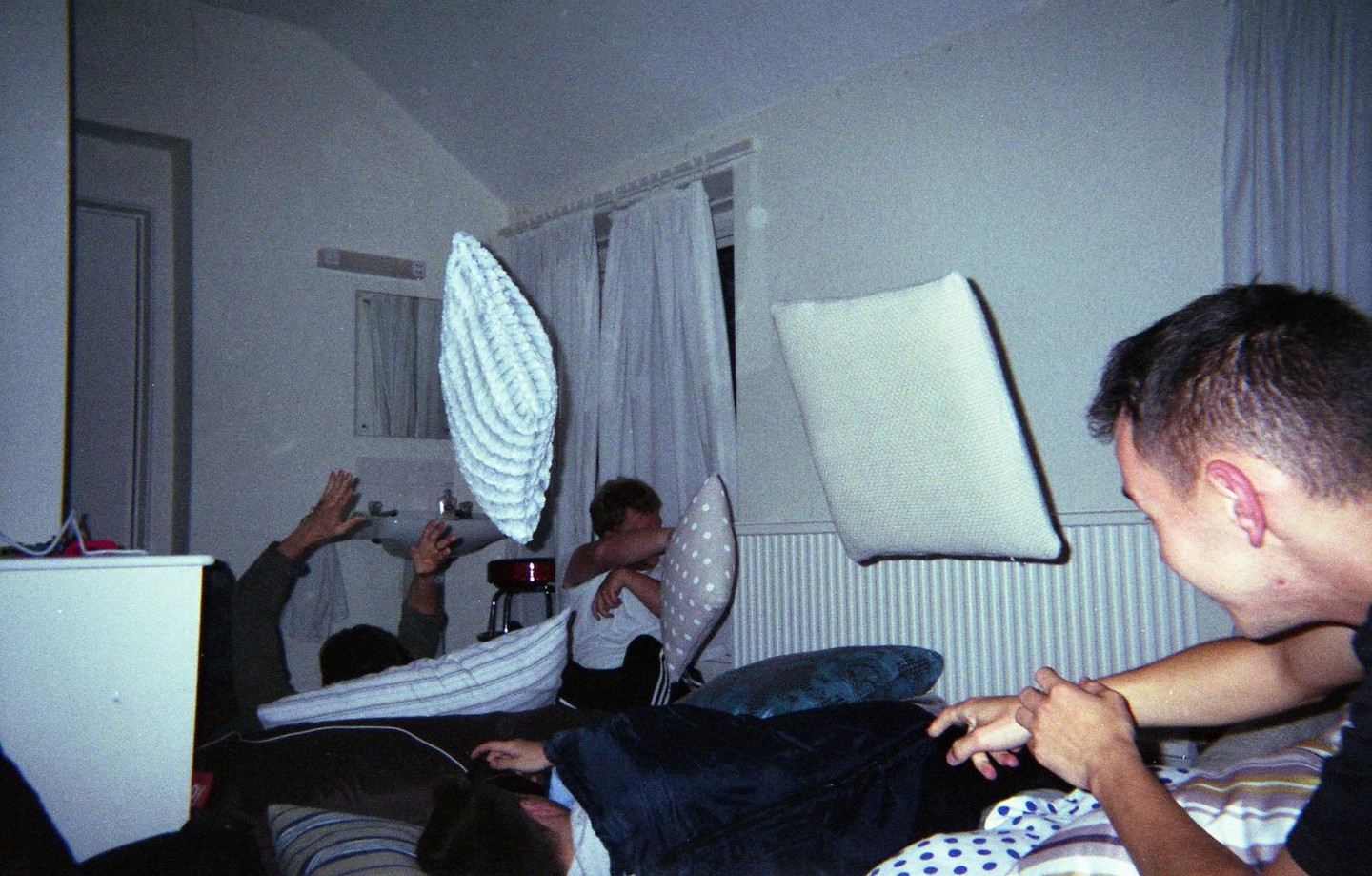 Three men are having a pillow fight in a bedroom.