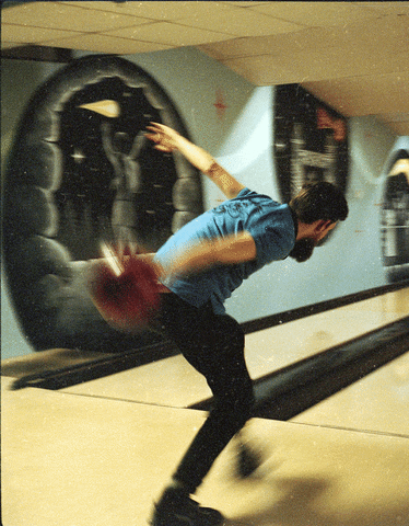 A man bowls a red bowling ball down an alley.