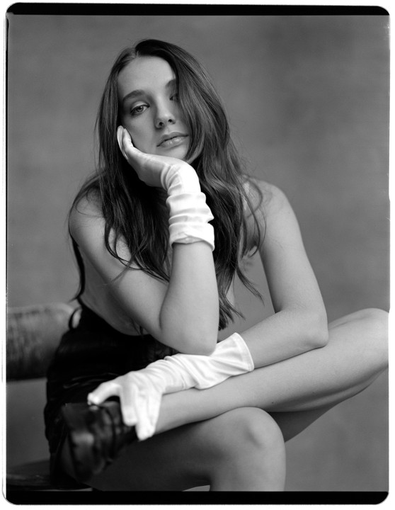 A woman wearing white gloves poses with her hand on her chin.
