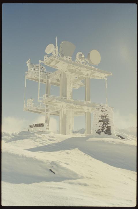 A snow-covered communication tower with multiple satellite dishes stands on a snowy mountain.