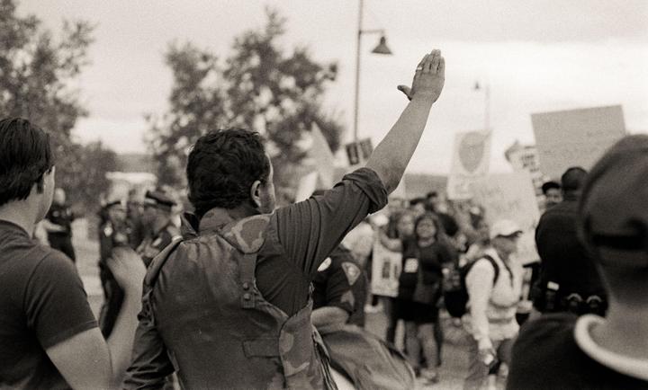 A man with his arm raised stands in a crowd of people, some holding signs.
