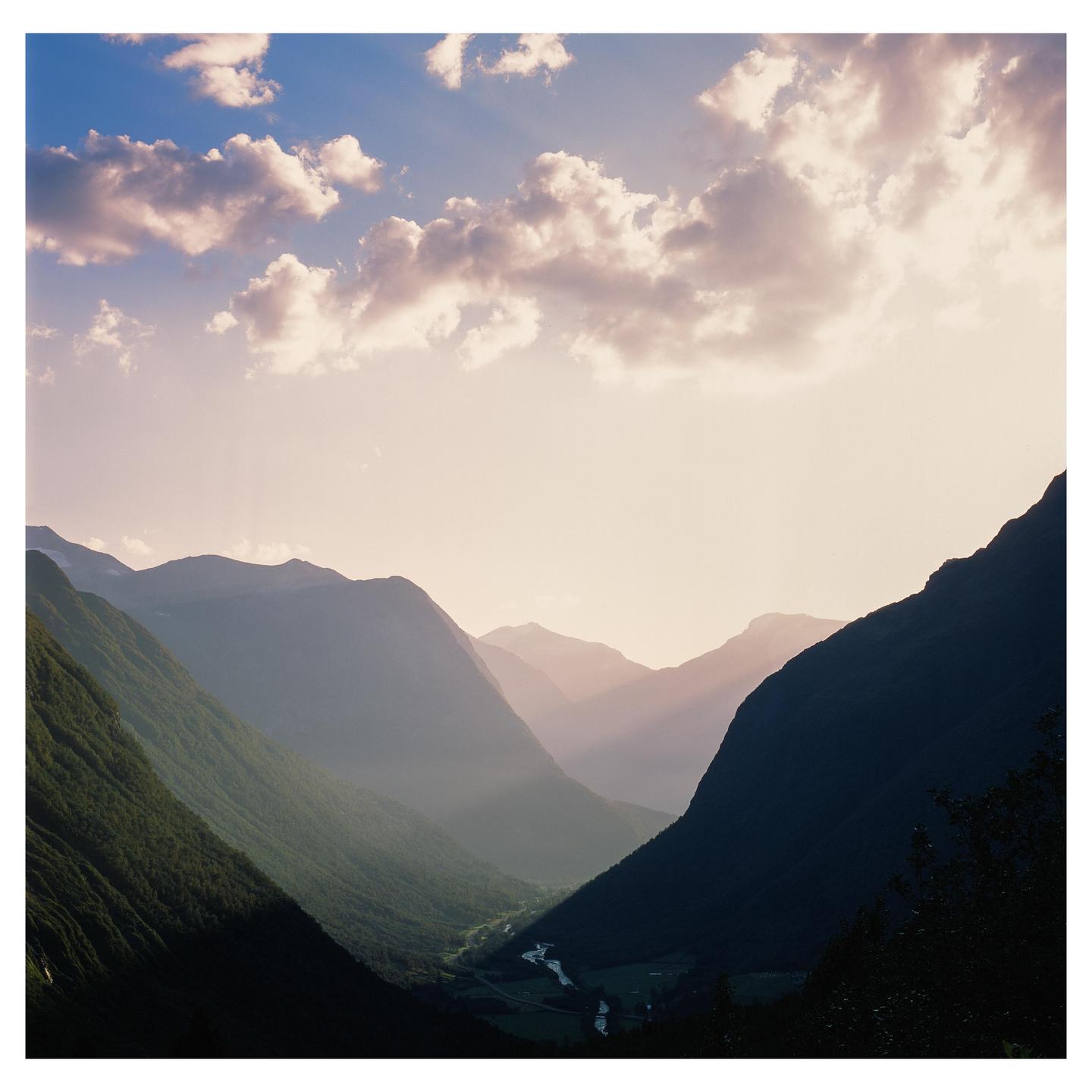 Sunlight streams through clouds into a valley with a river and mountains.