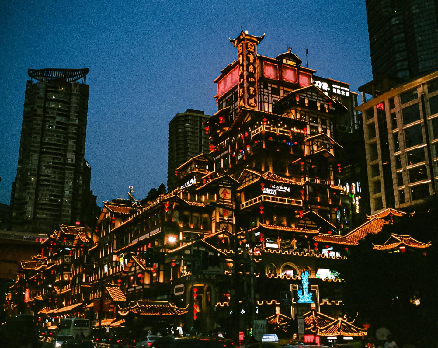 A multi-story building with traditional Chinese architecture is brightly lit at night, surrounded by modern skyscrapers.