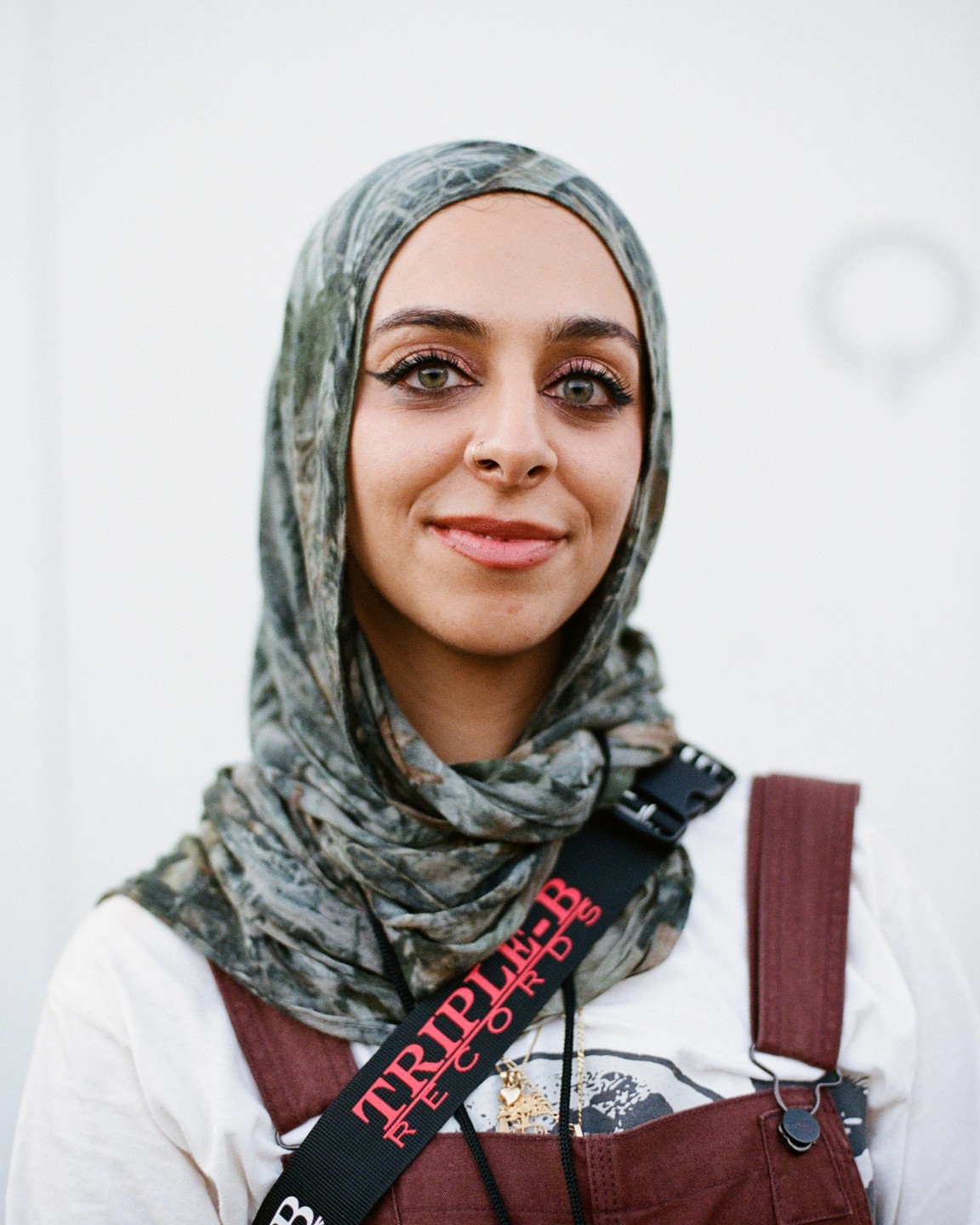 A woman wearing a patterned hijab and overalls smiles at the viewer.