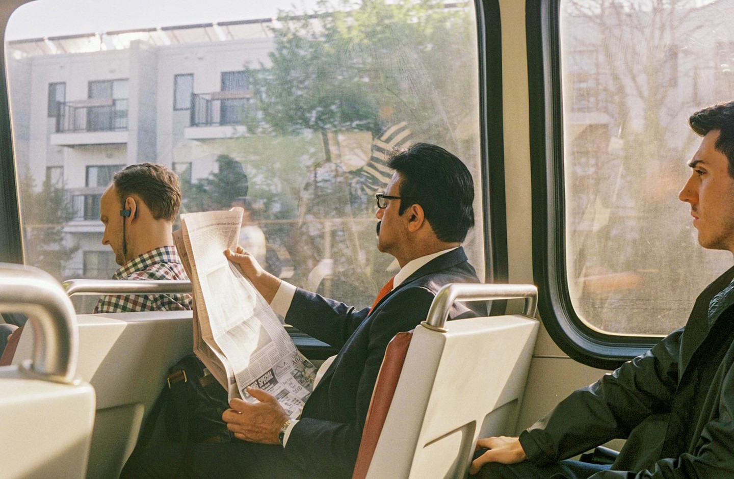 Three men are riding a metro train, one of whom is reading a newspaper.