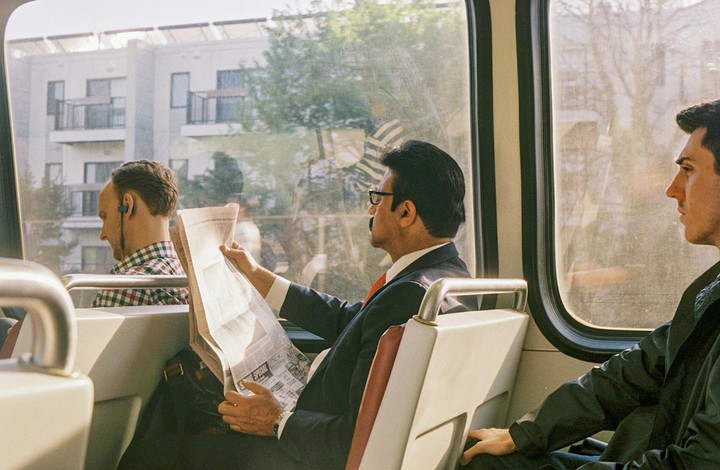 Three men are riding a metro train, one of whom is reading a newspaper.