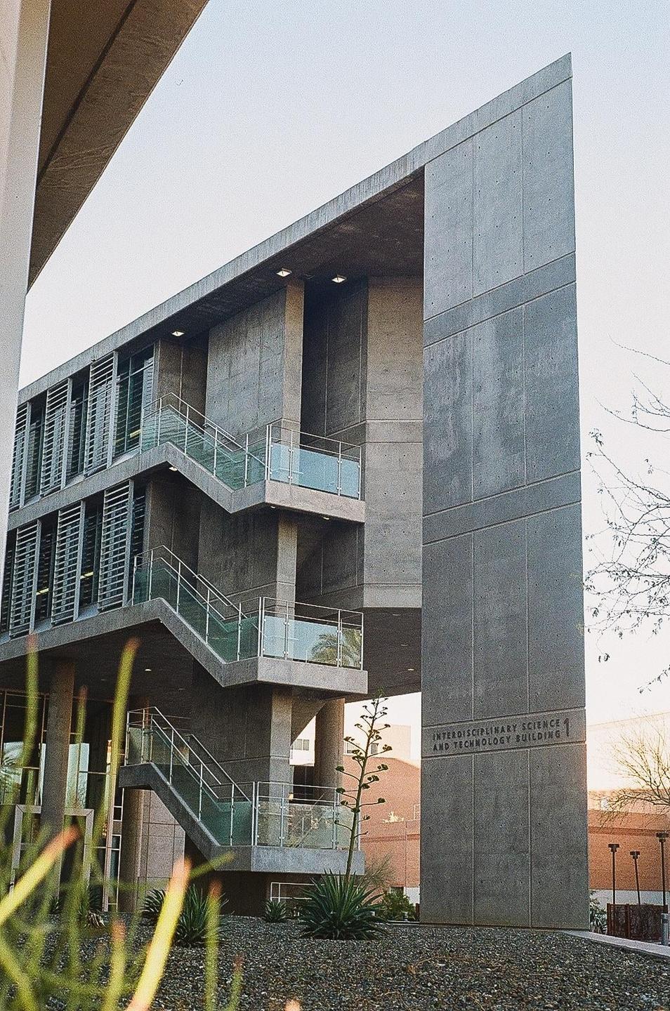 A concrete building with external staircases and glass railings is seen from a low angle.