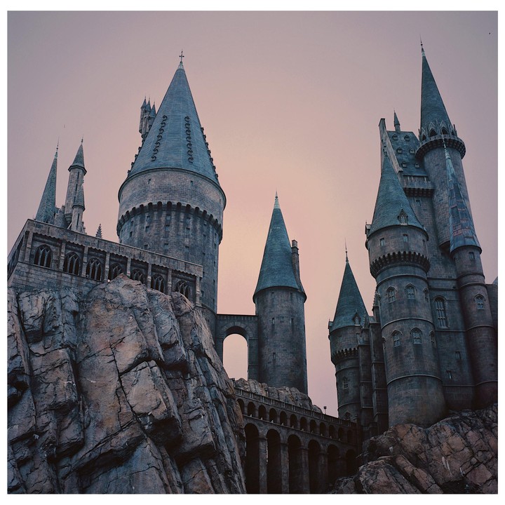 A large, dark castle with multiple turrets and spires stands against a pale sky, with rocky formations in the foreground.