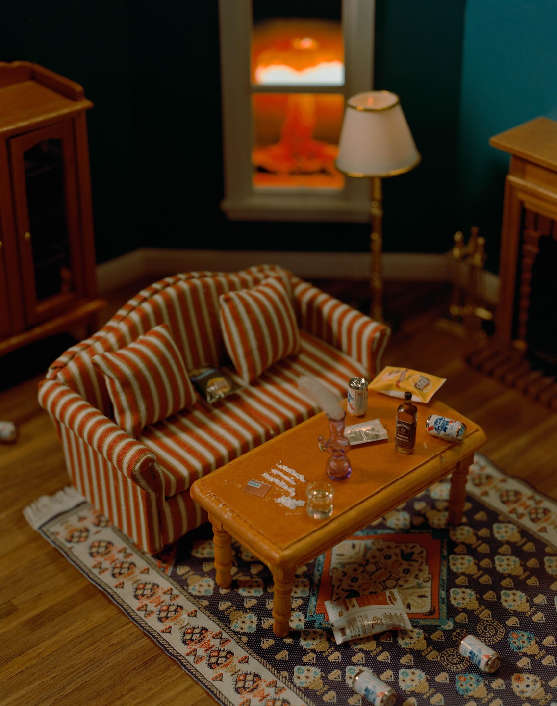 A miniature living room is shown with a striped couch, a coffee table with drug paraphernalia, and a window showing an explosion outside.