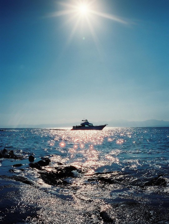A boat is visible on the sparkling water with the sun high in the sky.