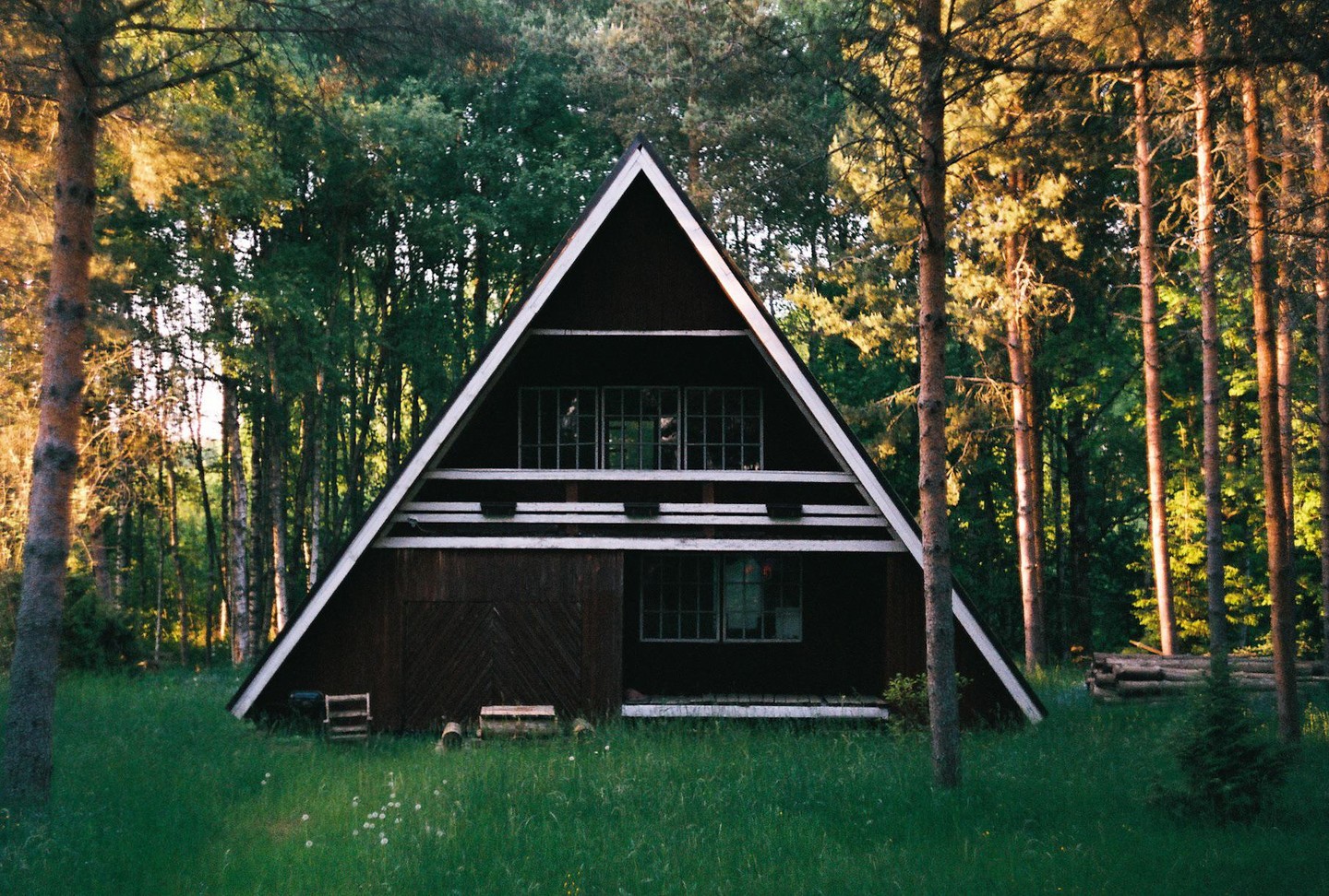 A-frame house stands in a grassy clearing surrounded by a forest.