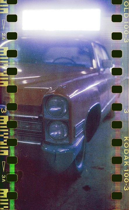 A vintage car with dual headlights is visible through a film strip border.