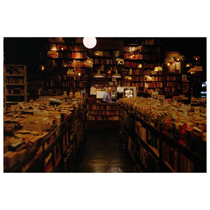 A man stands behind a counter in a bookstore filled with shelves of books.