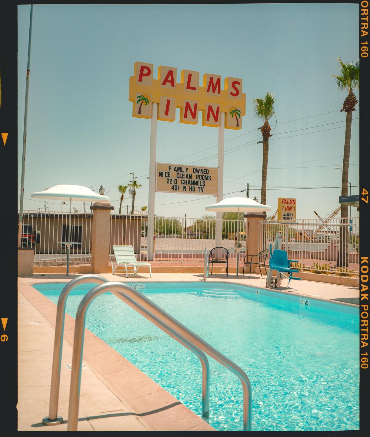 A swimming pool with a metal handrail is in the foreground, and a Palms Inn sign is in the background.