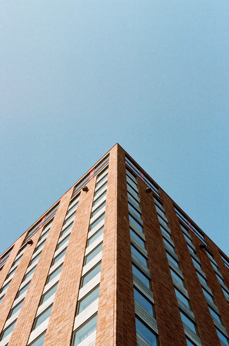 A tall brick building with many windows is photographed from a low angle against a clear blue sky.