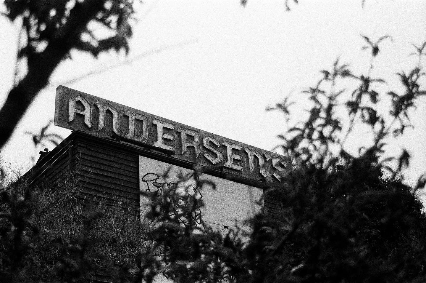A weathered sign for "ANDERSEN'S" sits atop a building, partially obscured by foliage.