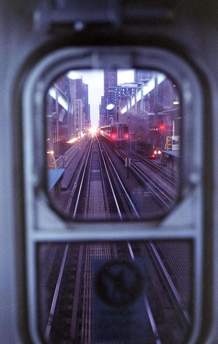A train is visible through a window, with city buildings and tracks stretching into the distance.
