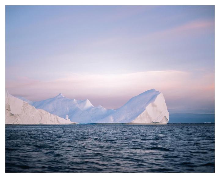 Icebergs float on the water under a pastel sky.