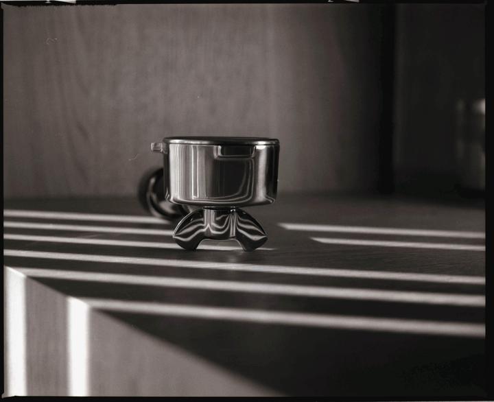 A metal espresso portafilter sits on a surface with strong shadows cast across it.