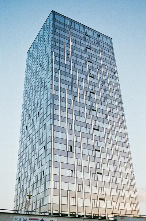 A tall, modern building with a glass facade stands against a clear sky.