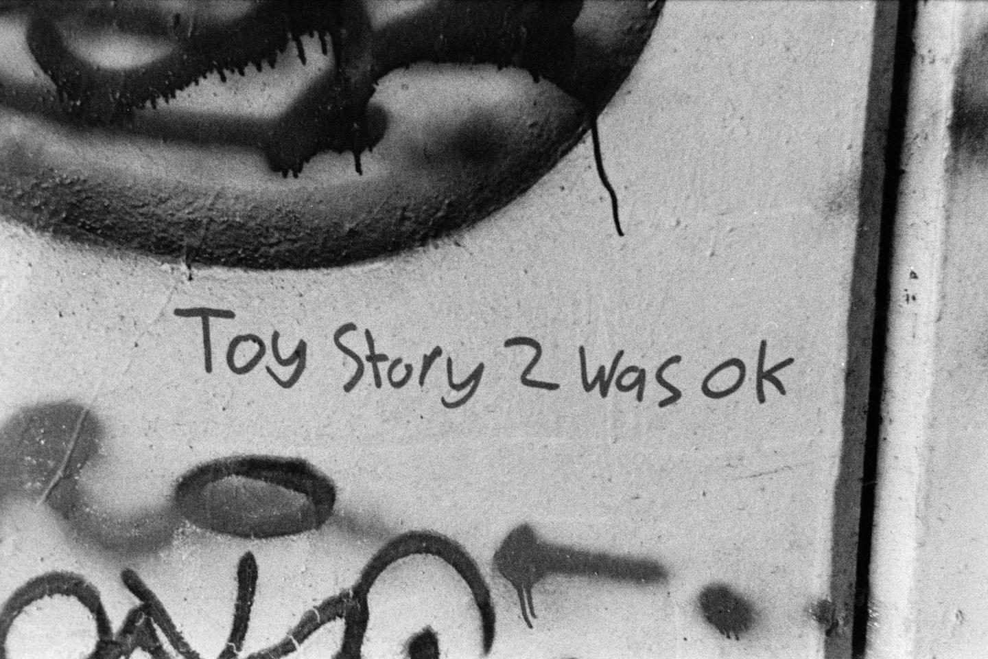 The phrase "Toy Story 2 was ok" is written on a wall with graffiti.