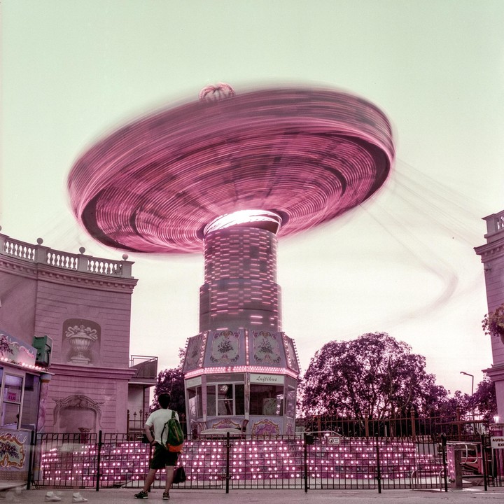 A man stands in front of a spinning carousel ride at a fairground.