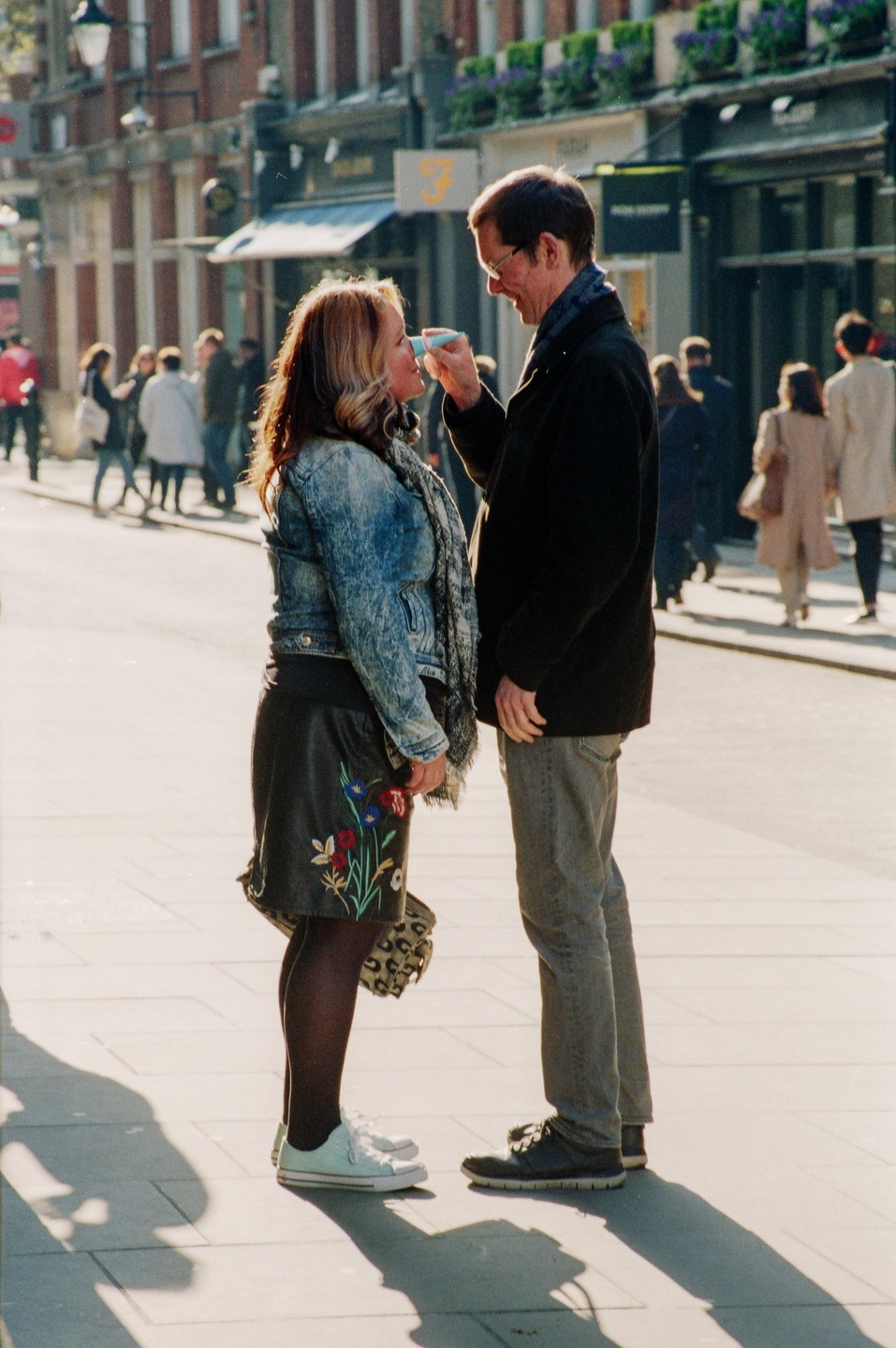 A man holds a small cup to a woman's mouth on a sunny street.