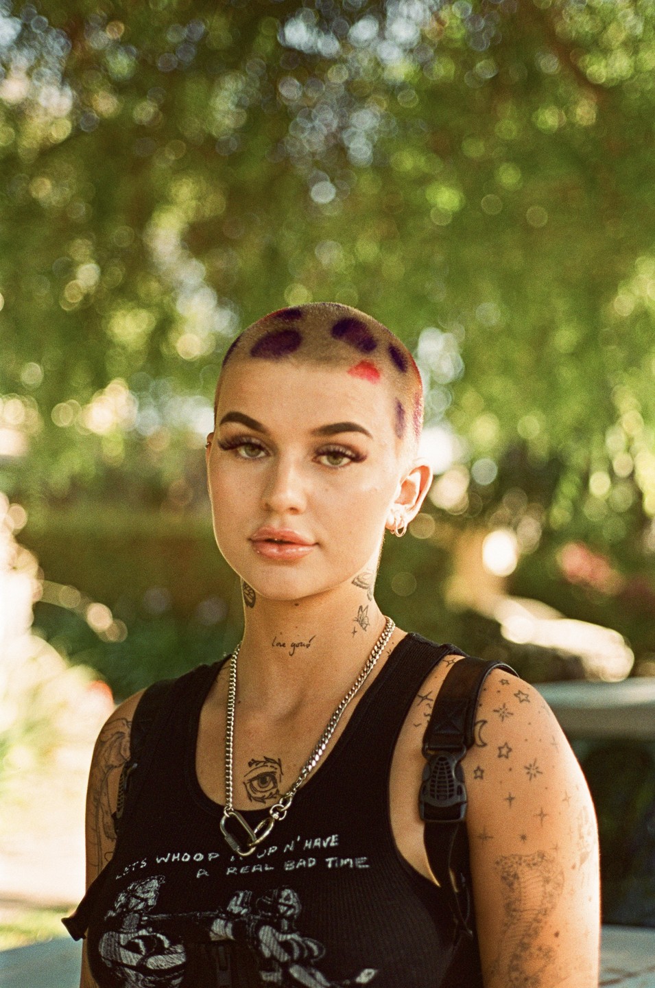 A woman with a shaved head and tattoos on her neck and arms looks at the viewer.