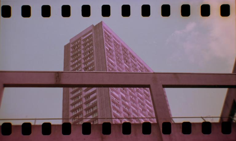 A tall building with many windows is visible behind a concrete structure, all under a pale sky.