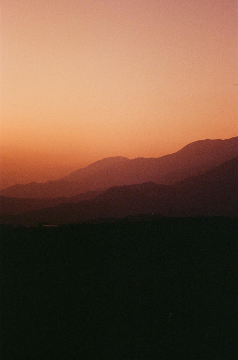 A landscape of layered mountains is silhouetted against a vibrant sunset sky.