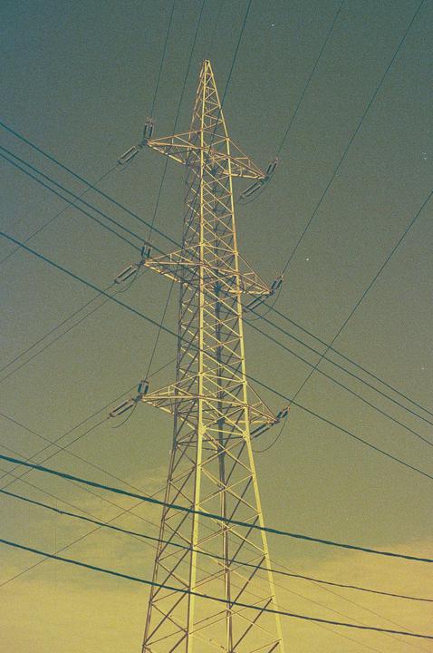 A tall metal electricity pylon stands against a hazy sky with numerous power lines stretching across the frame.