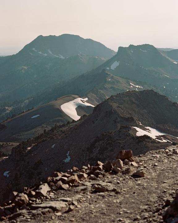 A mountain range with patches of snow is visible from a rocky foreground.