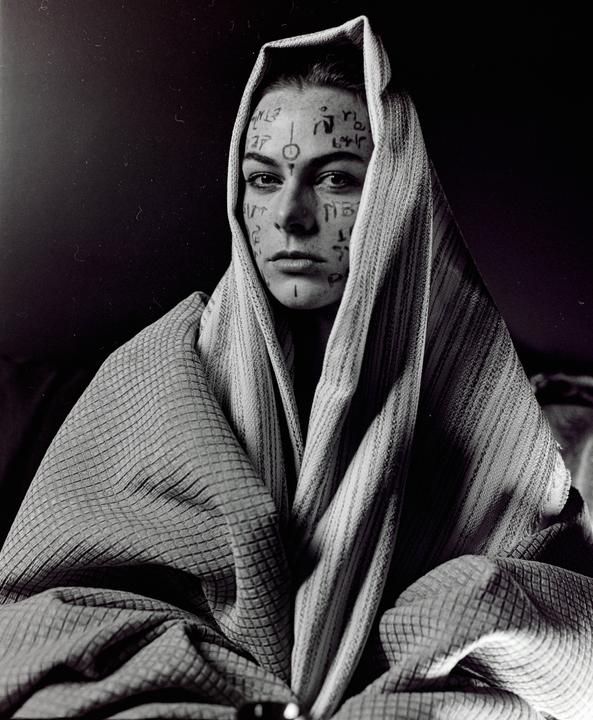 A woman with symbols drawn on her face is wrapped in a patterned fabric.
