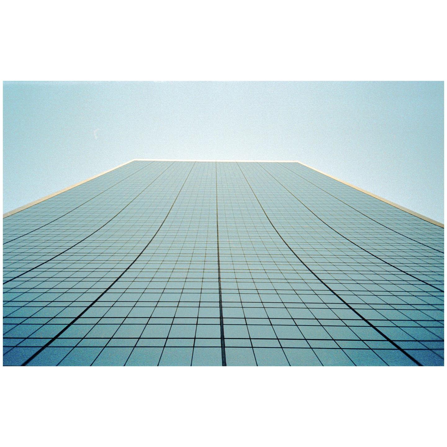 A tall glass building with a grid pattern on its facade rises towards a clear sky.