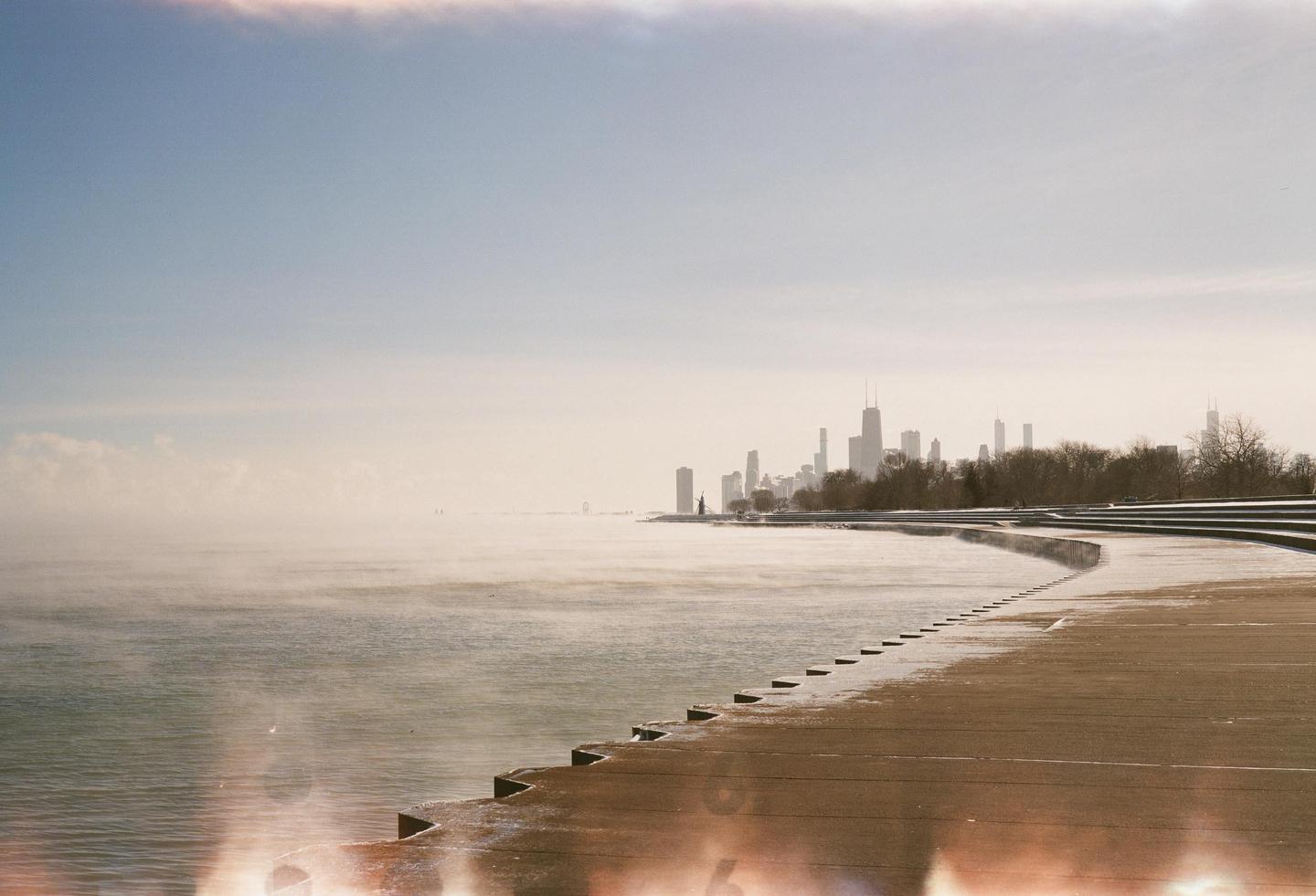 A city skyline is visible in the distance across a misty body of water with a curved concrete walkway in the foreground.
