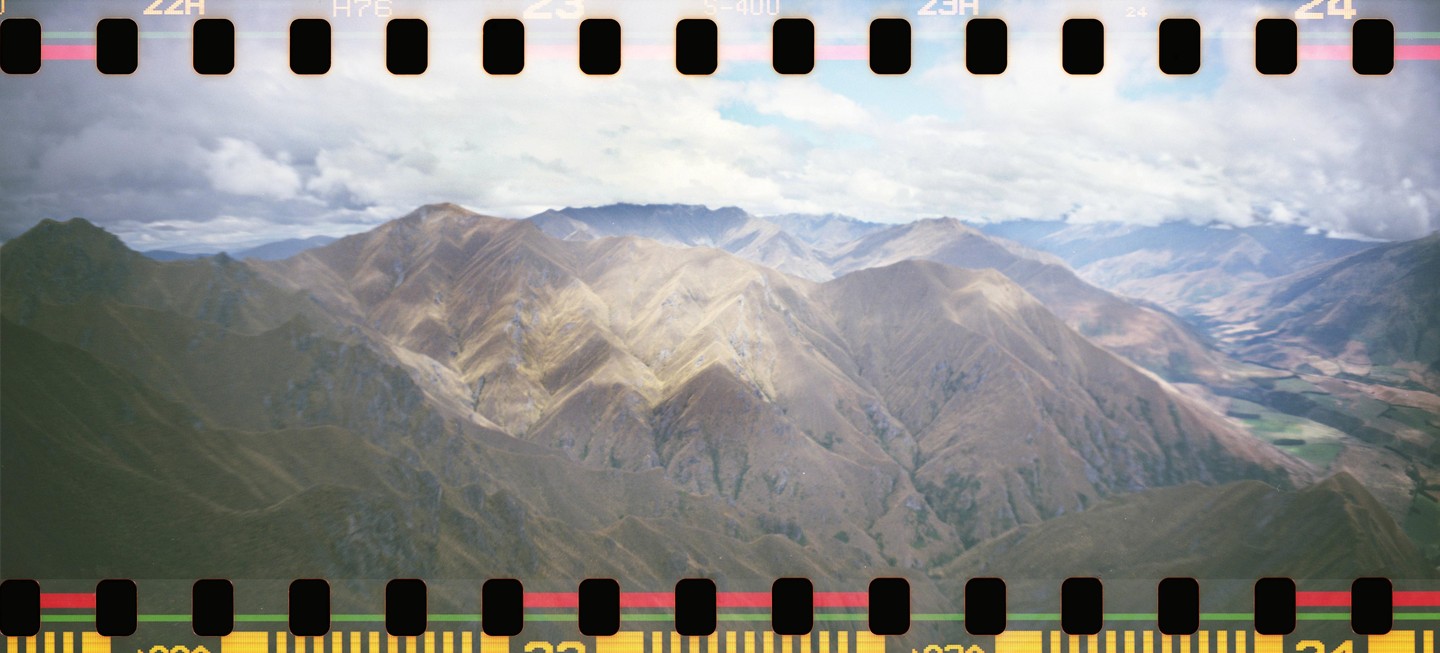 A panoramic landscape shows a vast mountain range under a cloudy sky, with a valley visible in the distance.