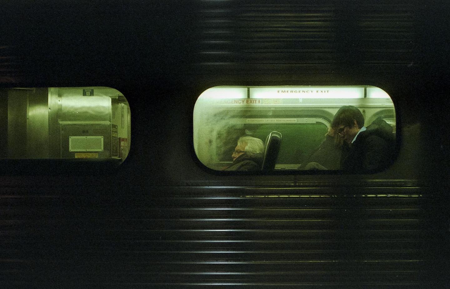 Two people are visible through the windows of a moving train at night.