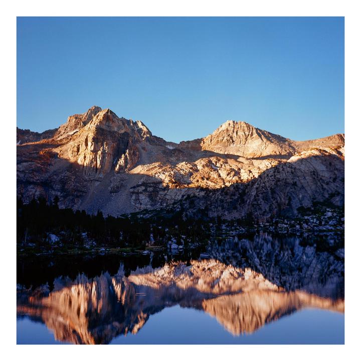 Mountains are reflected in a still lake under a clear sky.
