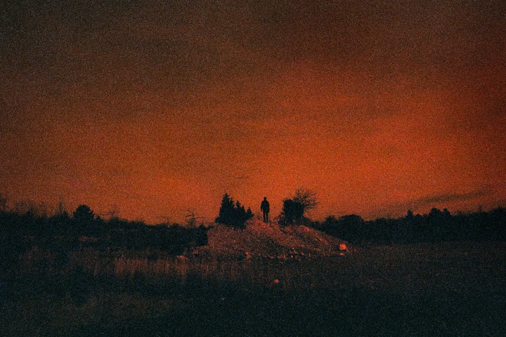 A lone man stands atop a hill silhouetted against a vibrant red sky.