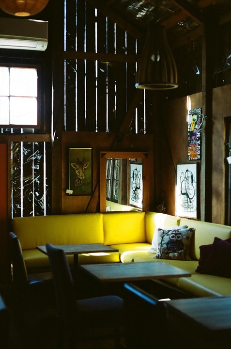 Sunlight streams into an empty cafe with yellow booth seating and wooden tables.