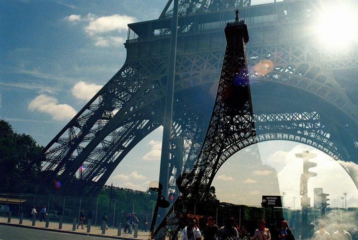 A double exposure shows the Eiffel Tower from two different perspectives, with people walking on the street below.