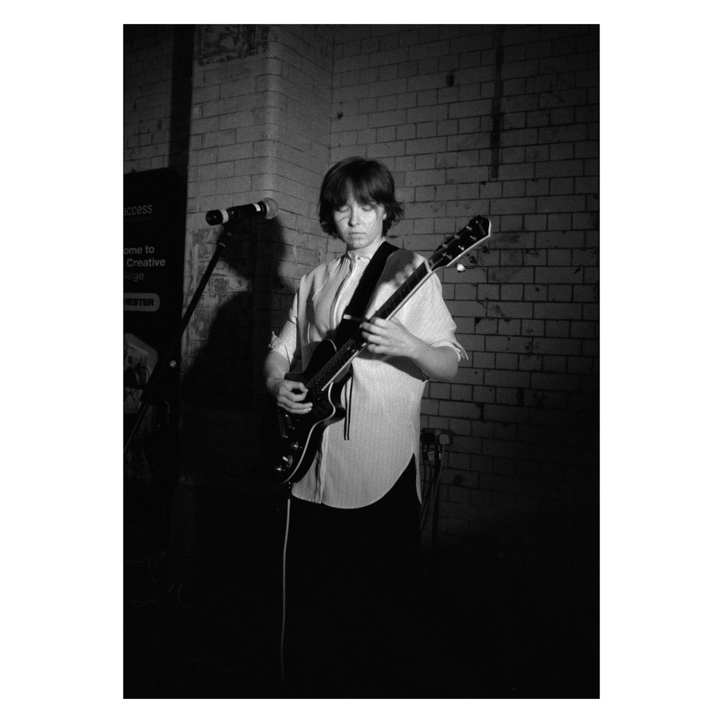 A woman plays an electric guitar in front of a brick wall.
