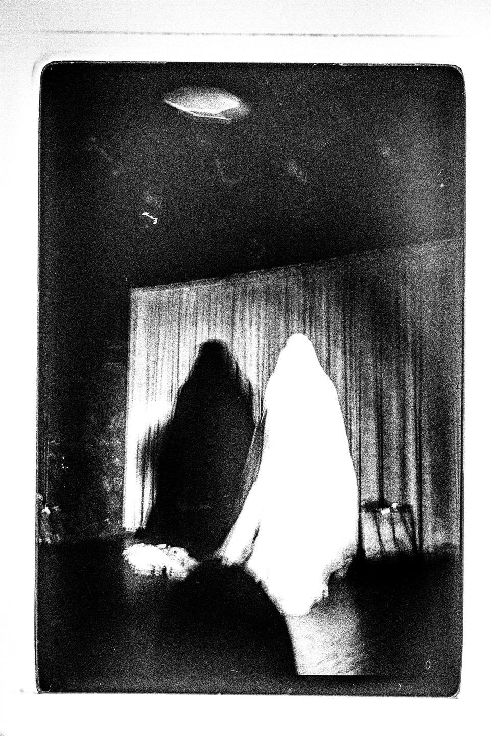 Two ghostly figures stand in front of a curtain, one dark and one light.