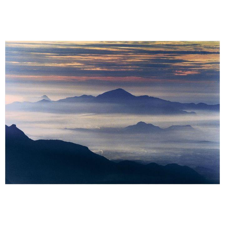 A mountain range is covered in fog under a dramatic sky.
